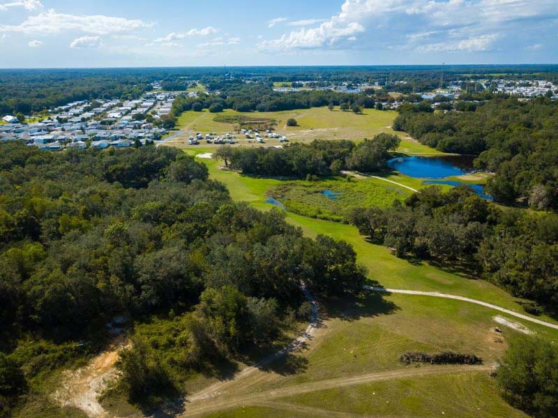 Bird's eye view of golf course with trees and pond, along with housing in distance